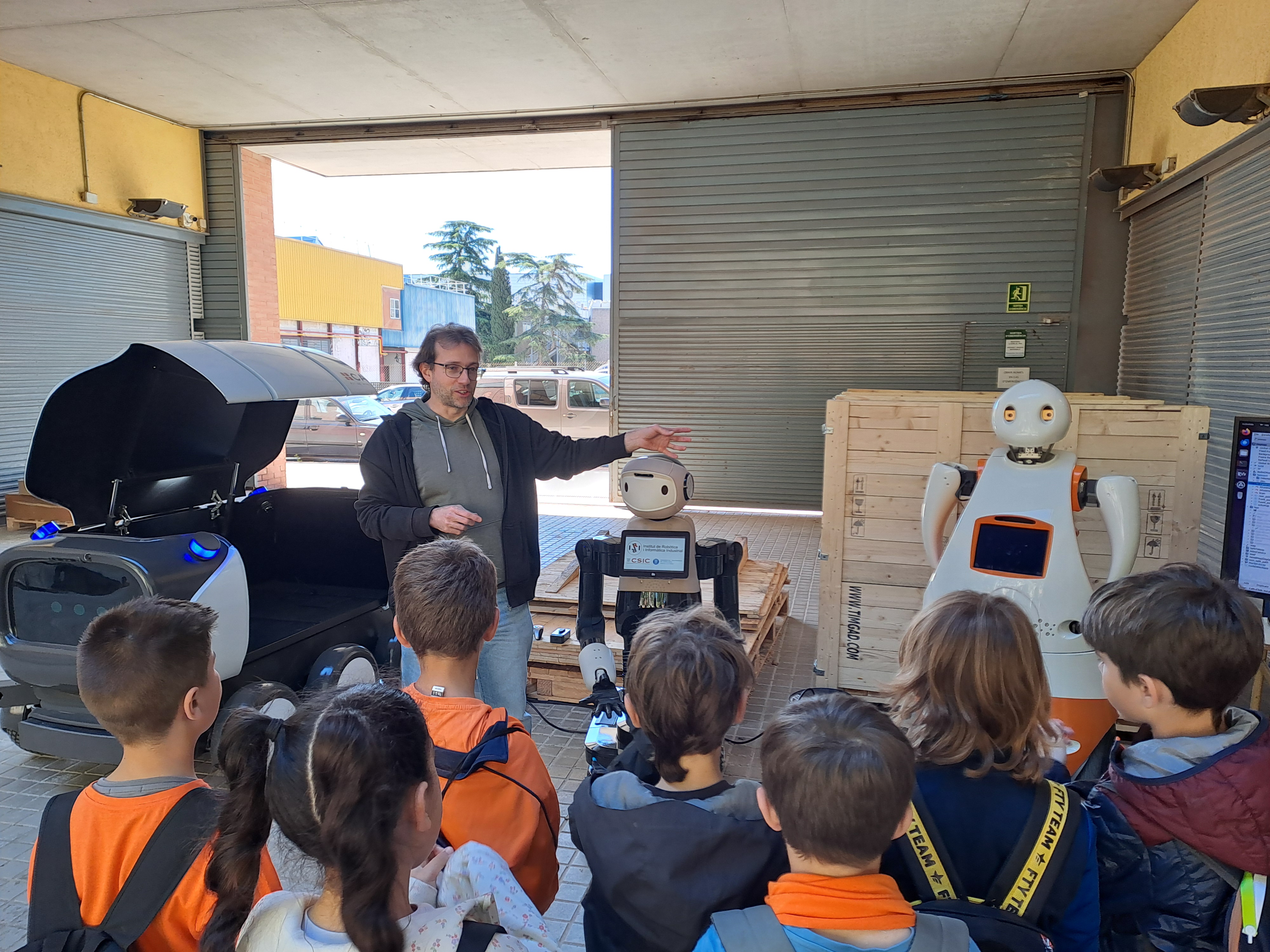 Foto de la Jornada de puertas abiertas al Instituto de Robótica e Informática Industrial (IRI, CSIC-UPC), con infantes viendo la presentación de dos robots.