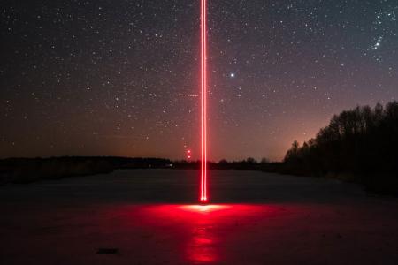 Paisaje de noche en el que sale de la tierra hacia el cielo un rayo láser rojo